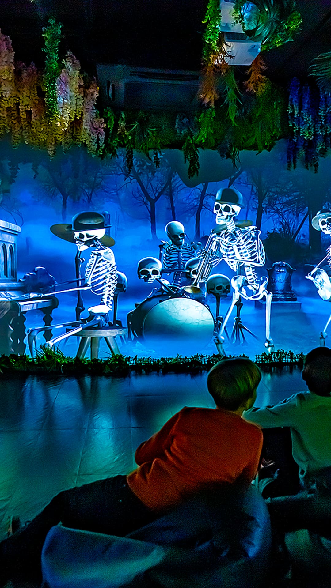 Two children watching a projected skeleton band play in a moonlit blue graveyard scene at Magic Room Barcelona