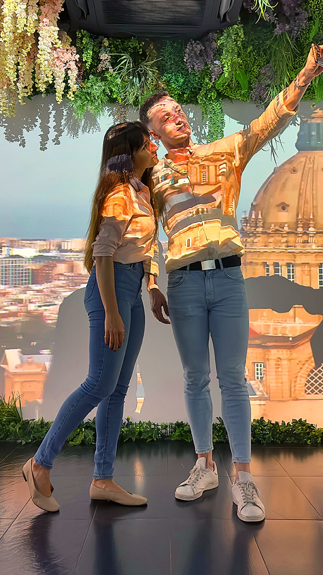 A couple taking a selfie as a projection of a Barcelona domed landmark and city skyline wraps across them and the wall at Magic Room Barcelona