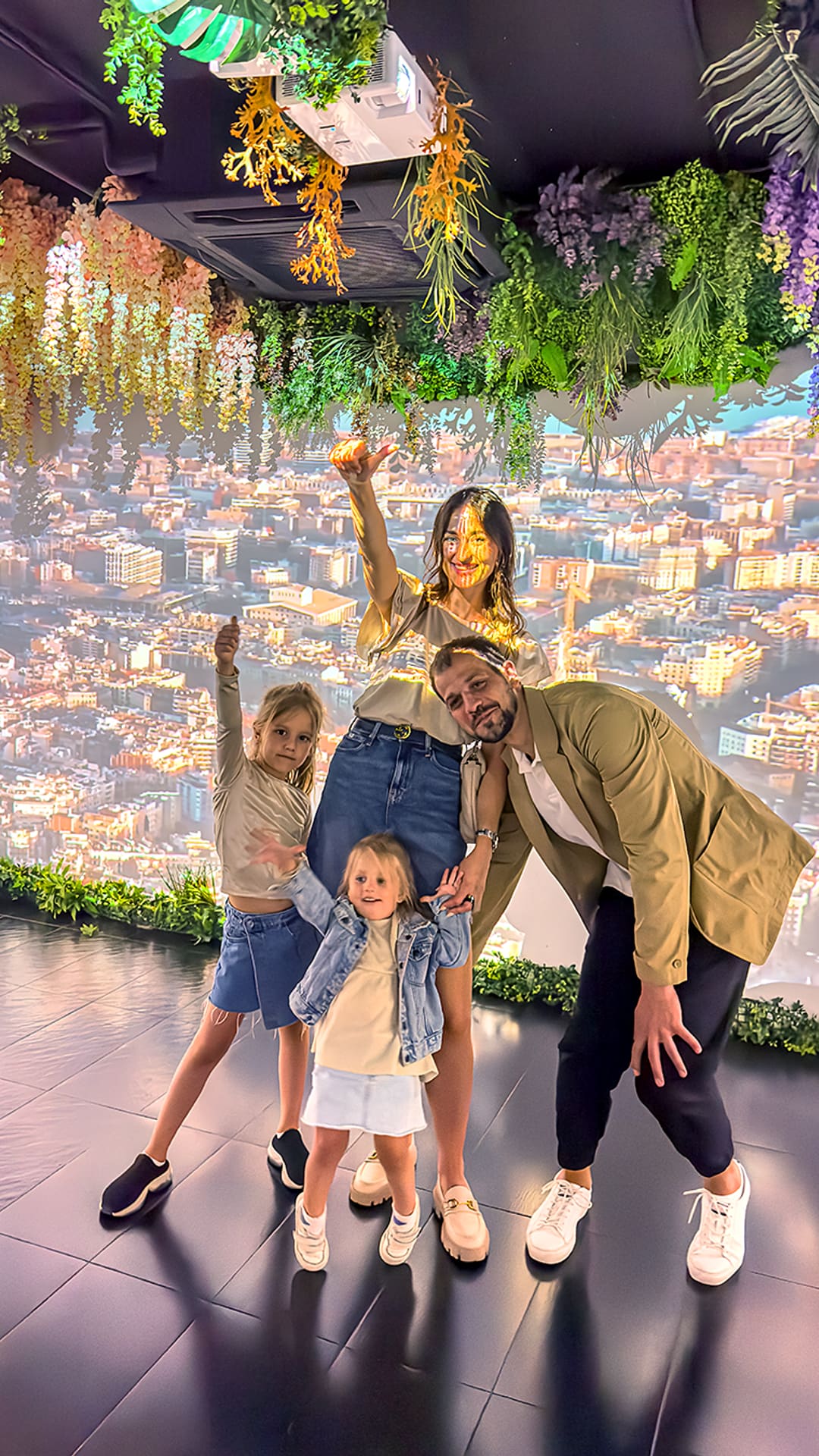 A family posing with arms raised as a projection of Barcelona's rooftops and hanging flowers wraps around the immersive room at Magic Room Barcelona